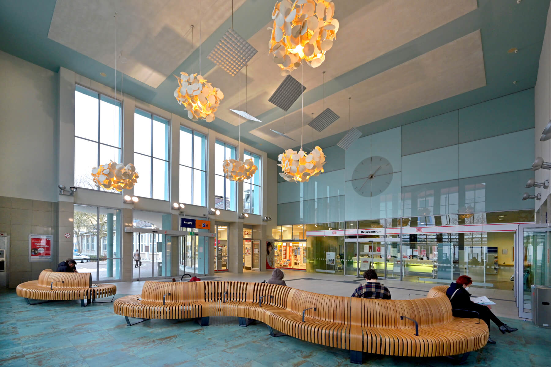 Eine modernisierte Bahnhofshalle, mittig Menschen auf einer Holzbank