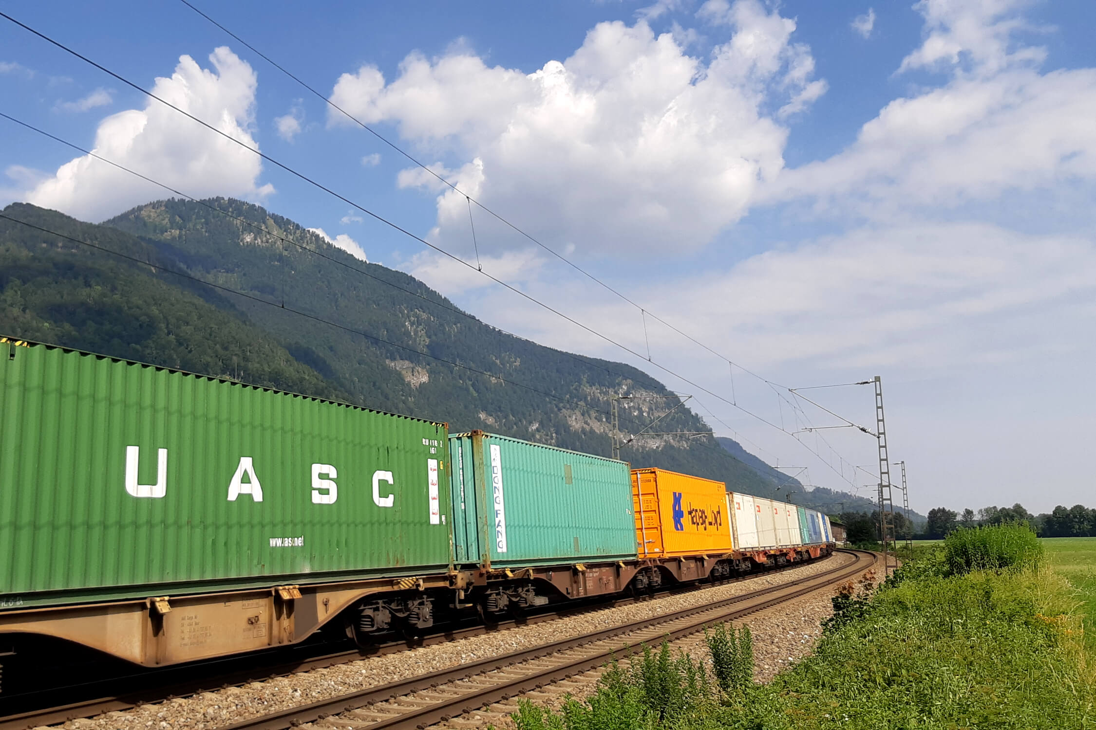 Ein Güterzug mit bunten Waggons fährt durch eine bergige Landschaft